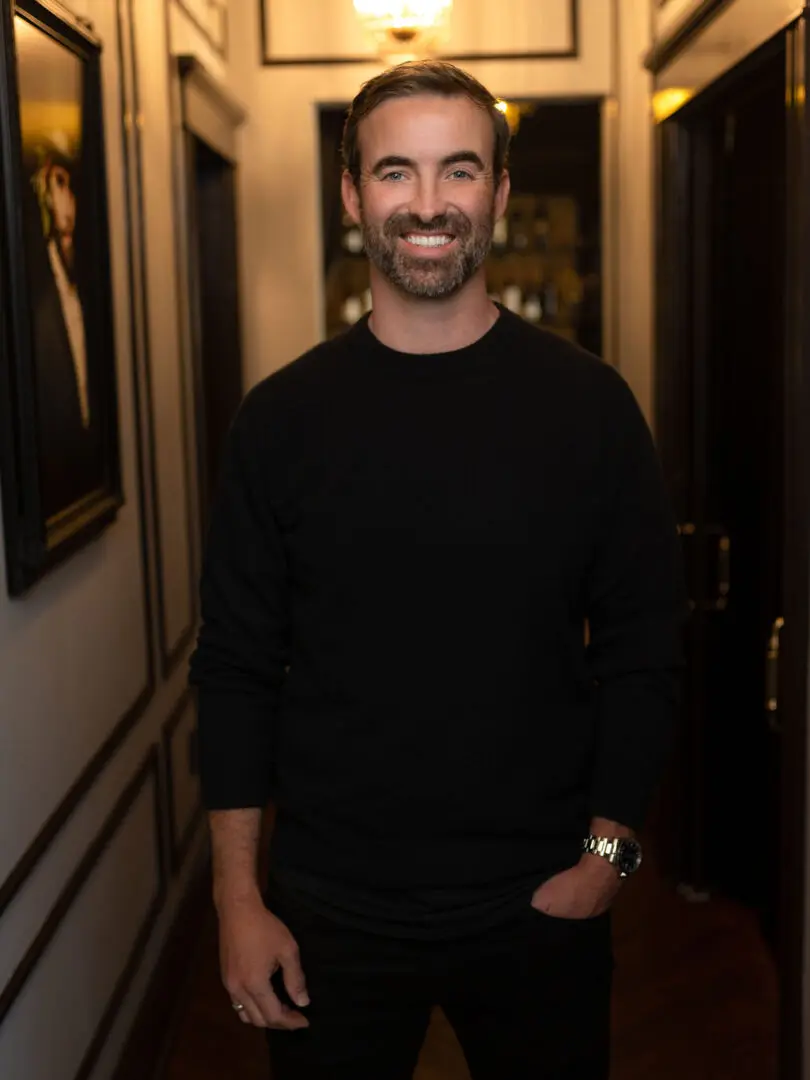 A man in black shirt standing next to wall.